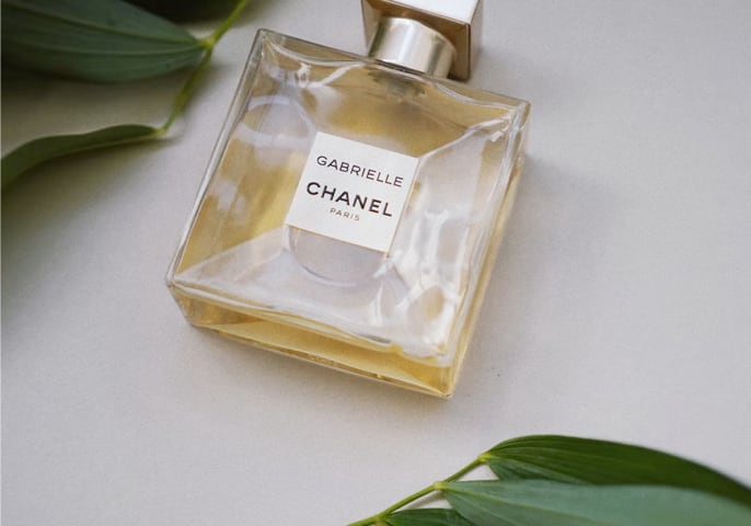 Glass Chanel perfume bottle on white surface with decorative leaves around it
